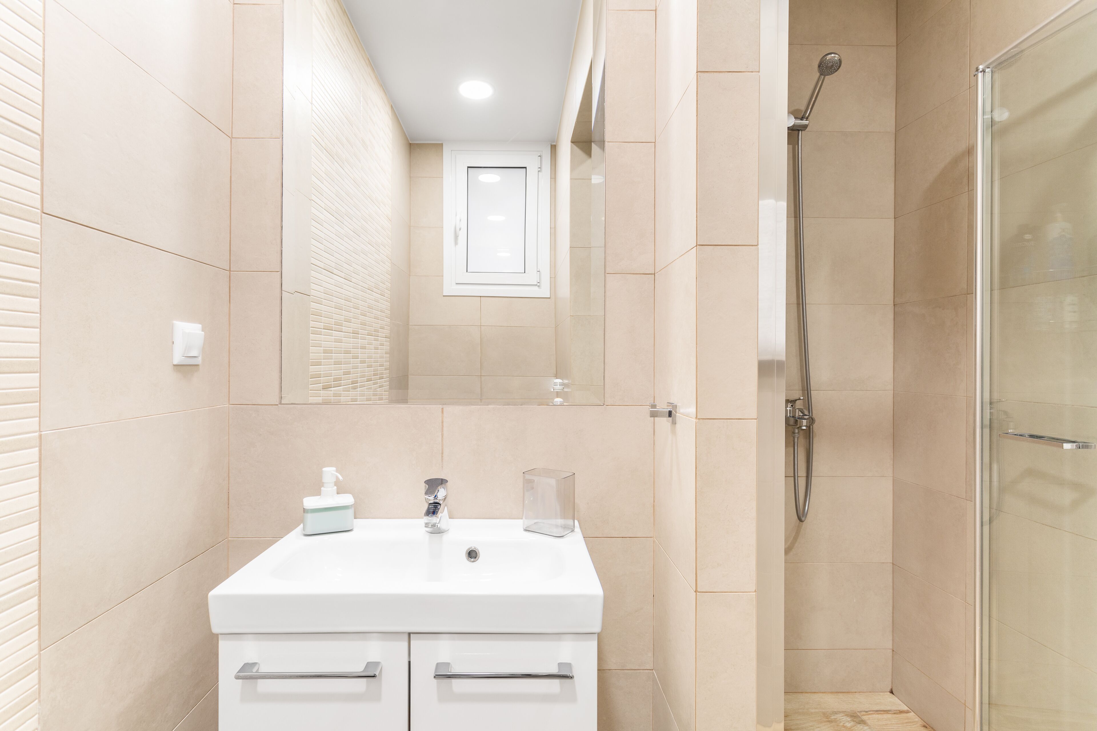 Un baño moderno con lavamanos blanco, espejo y cabina de ducha de vidrio.