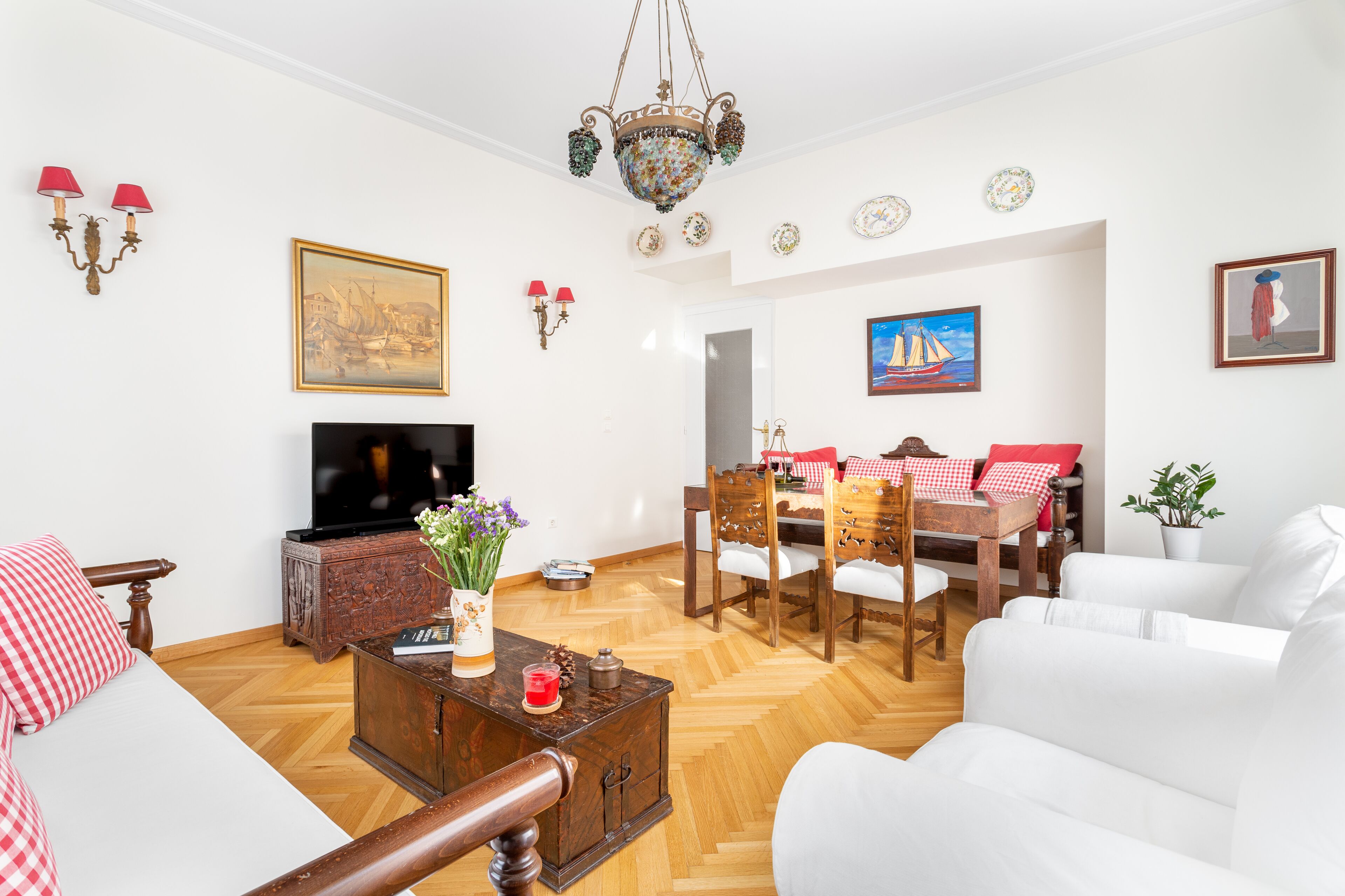A living room with a TV, wooden furniture, a chandelier, and artwork on the walls.