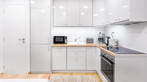 A modern kitchen with white cabinets, a microwave, toaster, coffee maker, and a stove. - Athens Squared Lofts (Athens)
