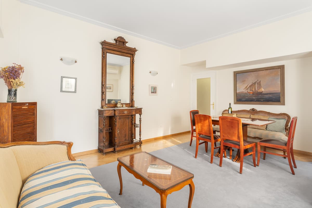 A living room with a sofa, a coffee table, a dining table with chairs, a wooden cabinet, and a painting on the wall.