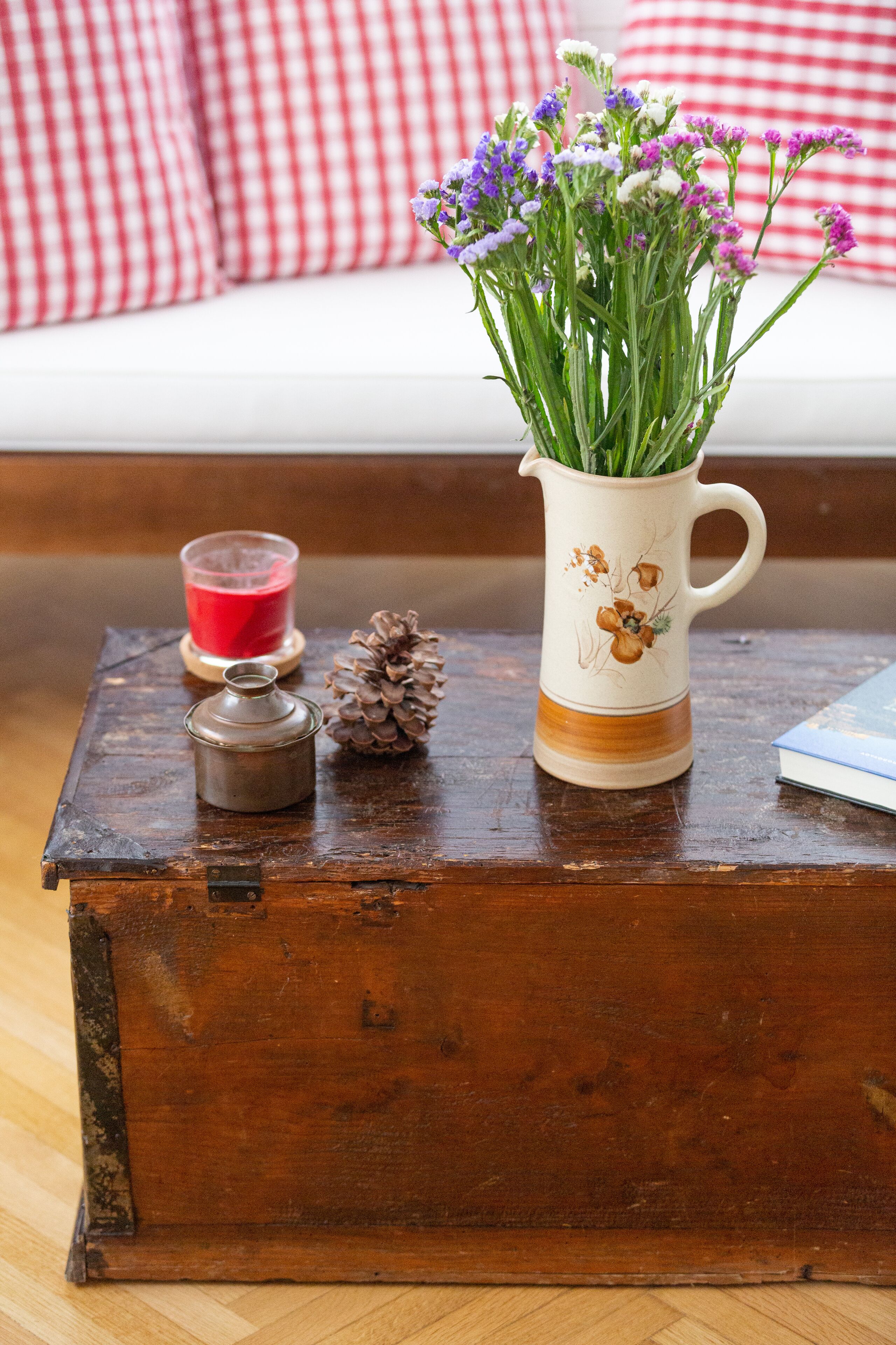A wooden chest with a vase of flowers, a candle, and a pine cone on a wooden table.