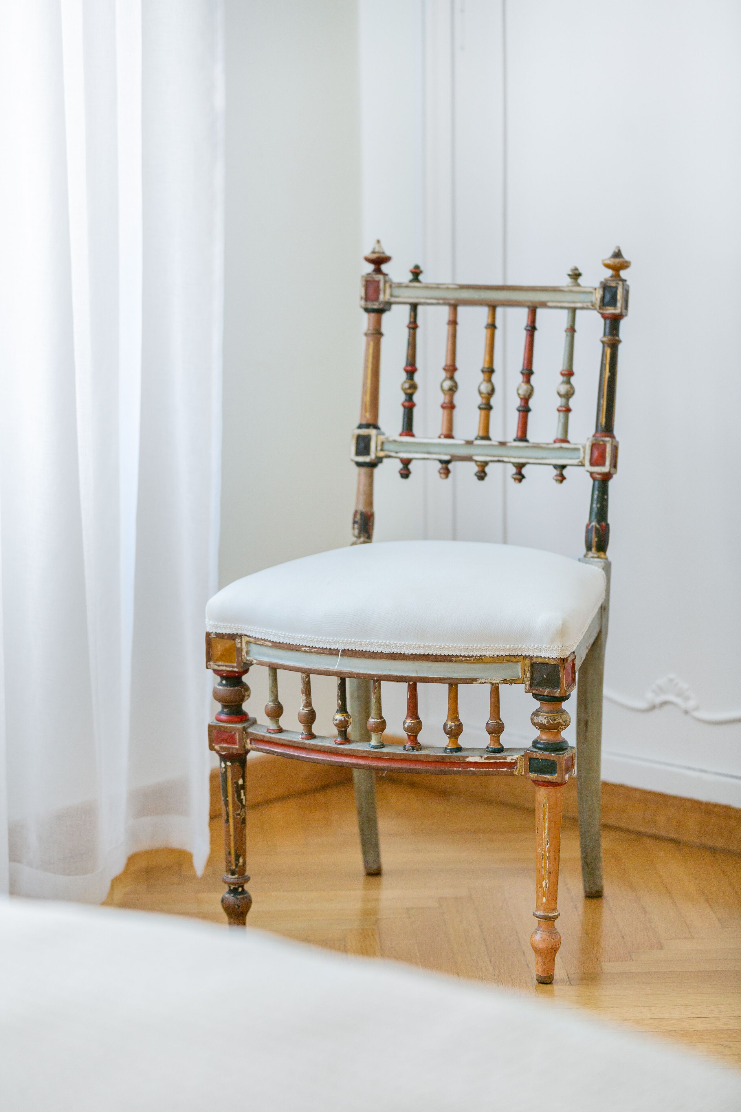 A vintage chair with a white cushion, wooden legs, and ornate metal accents.