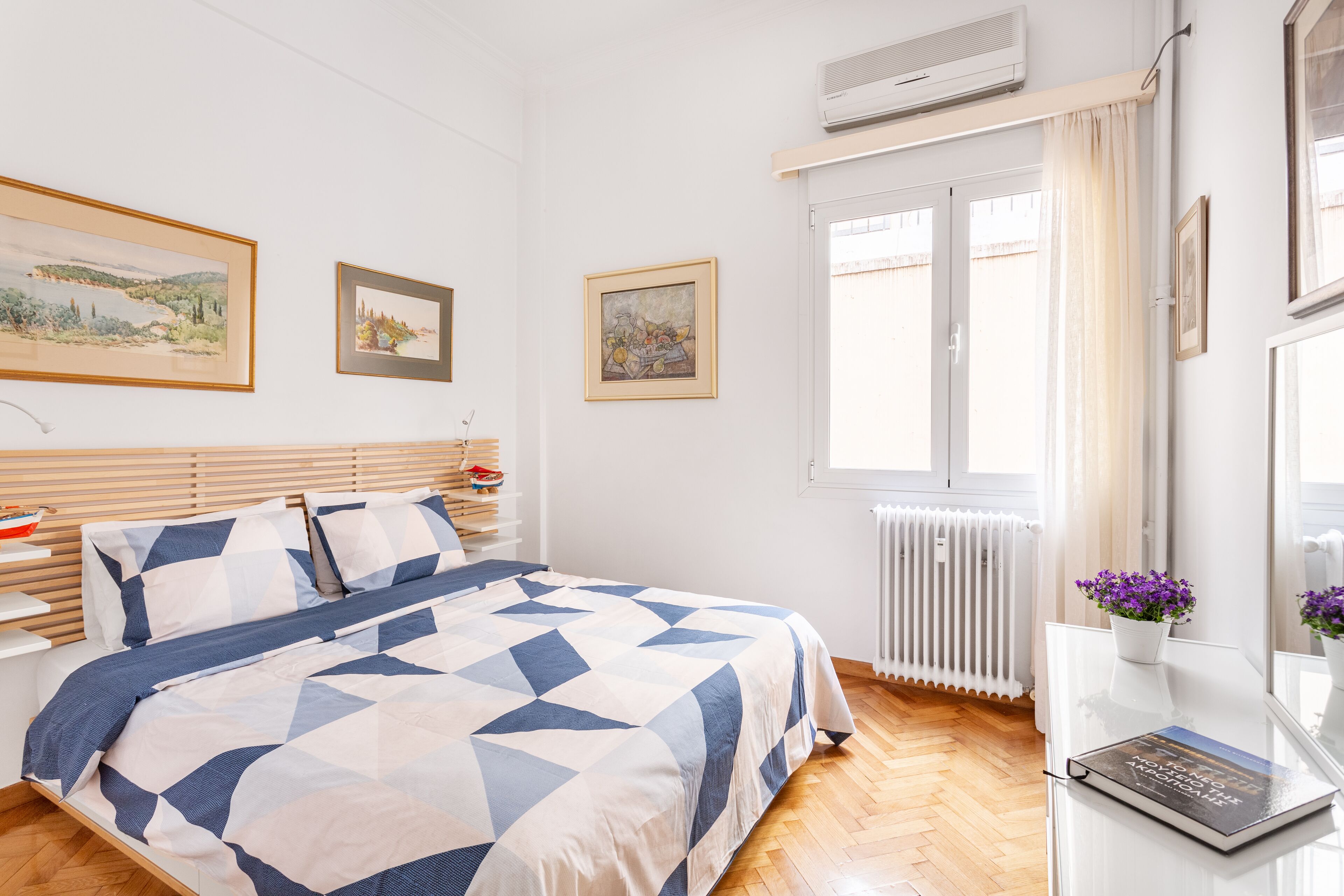 A bedroom with a bed, a bedside table, a window with curtains, and a radiator.