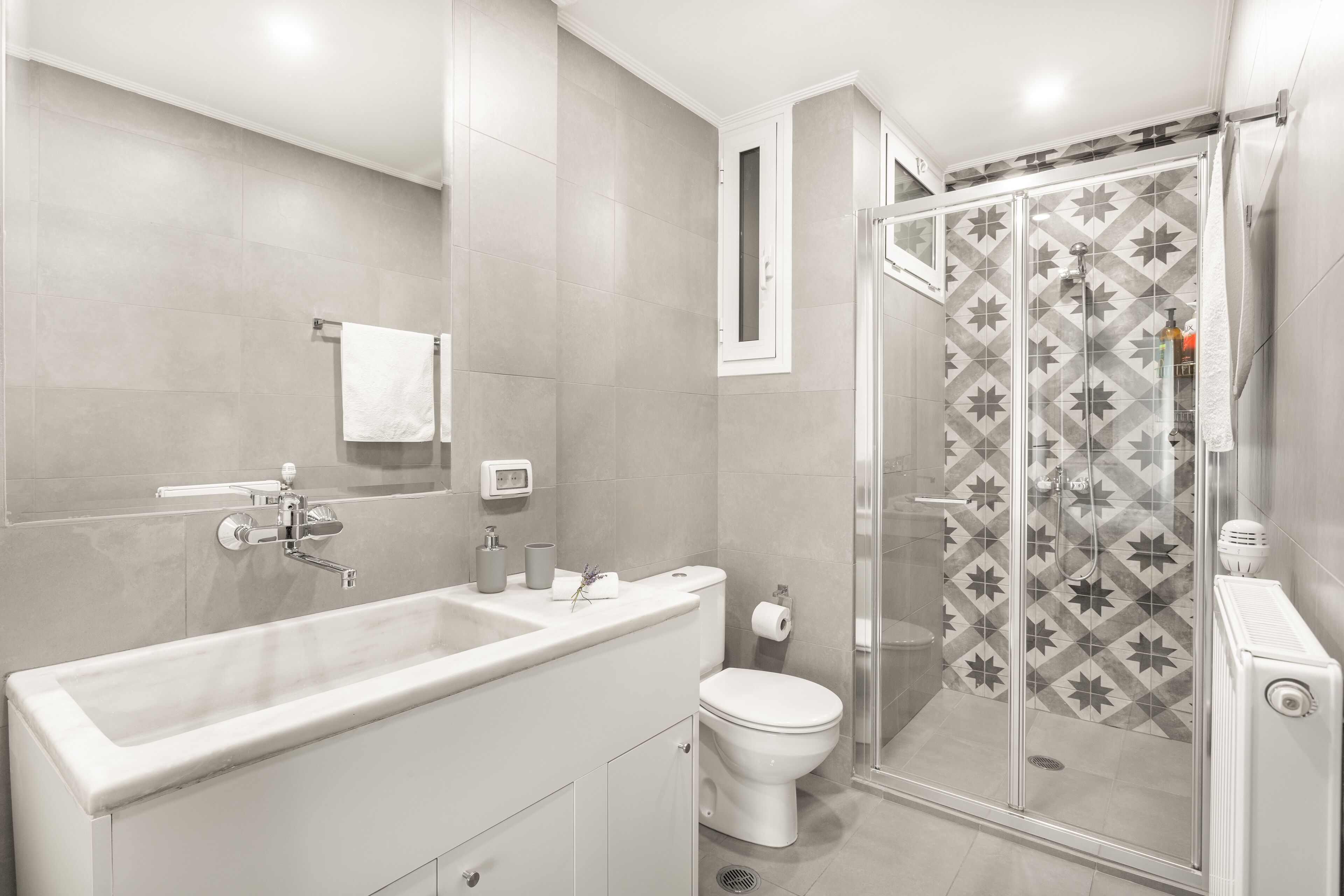 A modern bathroom with a large white bathtub, a toilet, and a shower area with patterned tiles.