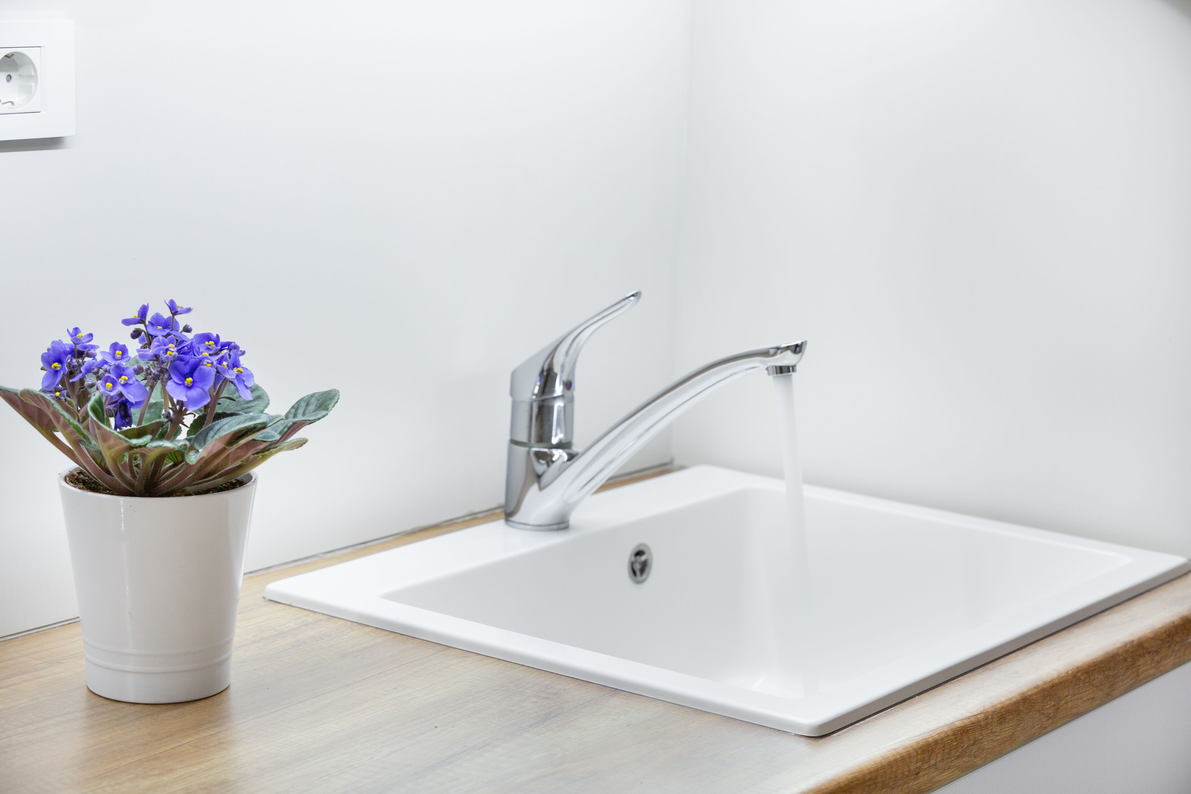 A white bathroom sink with a modern faucet and a potted plant with purple flowers.