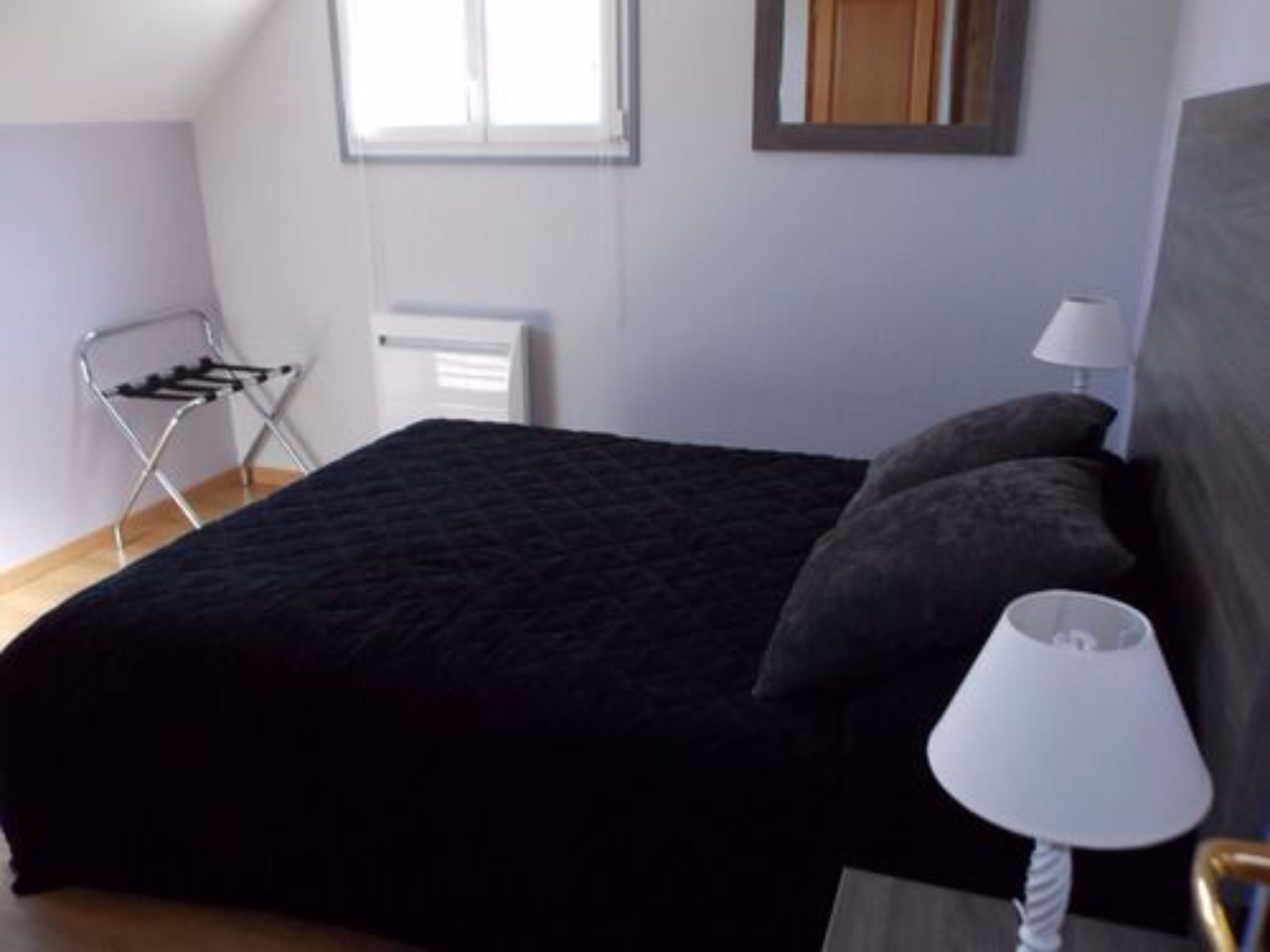 Een slaapkamer met een bed, nachtkastje, lamp, radiator en raam.