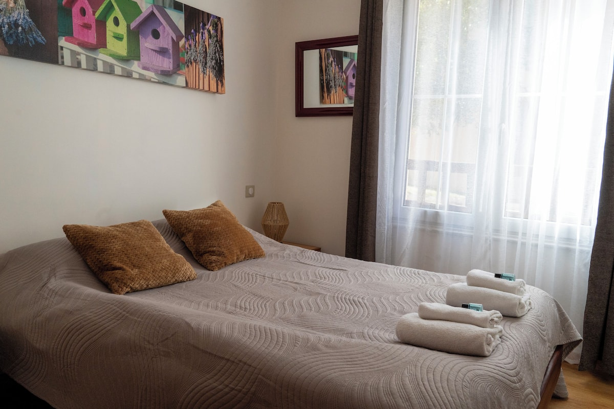 A neatly made bed with a textured bedspread, two brown pillows, and a set of towels.