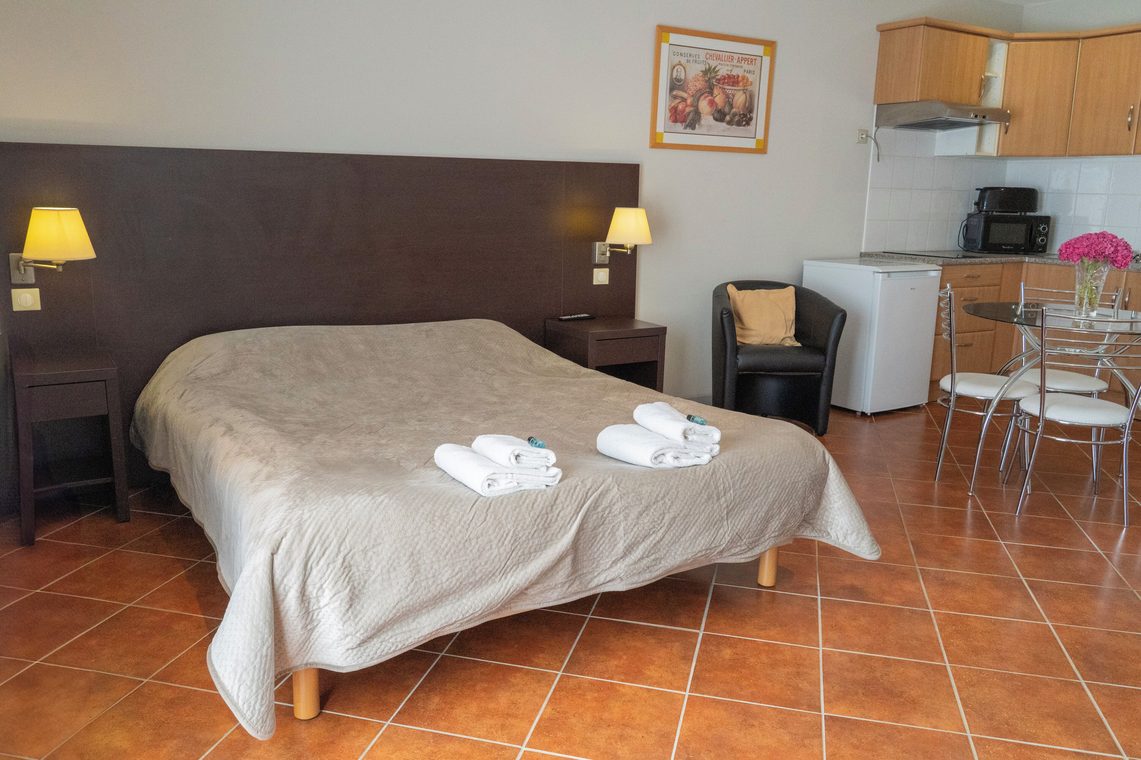 Ein Hotelzimmer mit einem Bett, zwei Nachttischlampen, einem kleinen Tisch mit Stühlen, einer Mikrowelle und einem Kühlschrank.