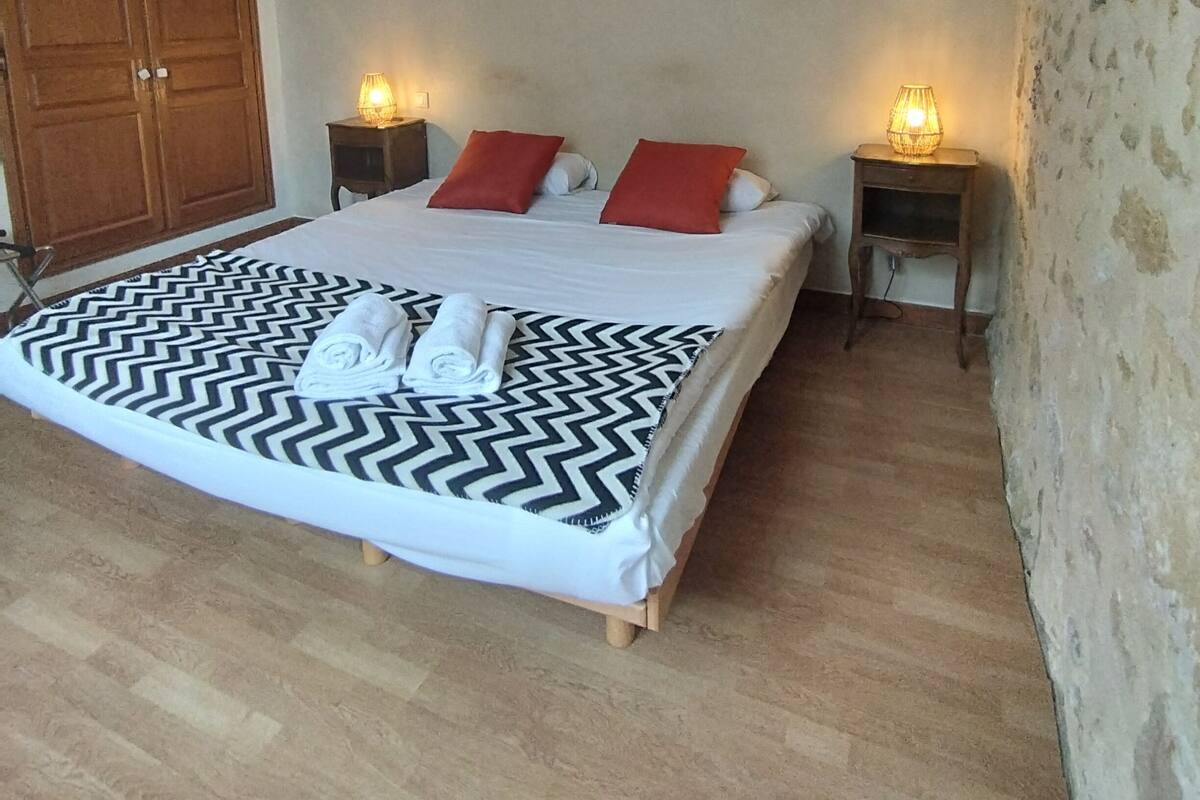 A bedroom with a large bed, two bedside tables with lamps, a wooden wardrobe, and a textured wall.
