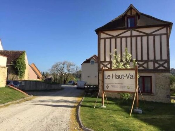 A traditional half-timbered building named Le Haut-Val with a signboard, surrounded by a rural setting with a gravel road and greenery. - Le Haut-Val résidence (Belleme)