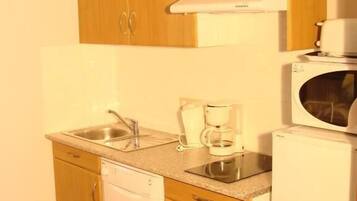 Kompakti keittiö, jossa on puukehikoiset kaapit, sisäänrakennettu astianpesukone, mikroaaltouuni ja kahvinkeitin.
