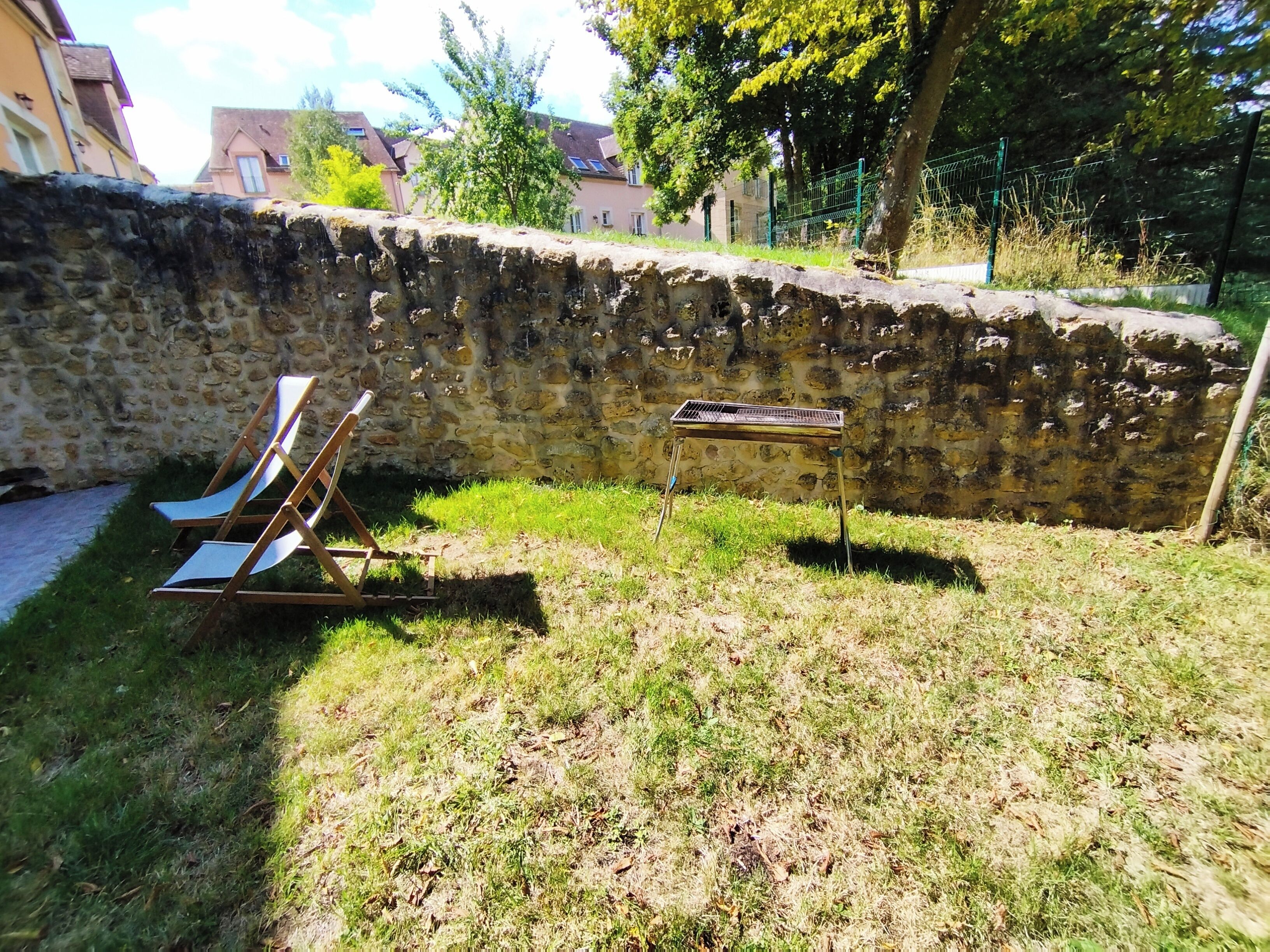 Eine steine Mauer, ein Metallgitter und ein Holzstuhl auf einer Rasenfläche.