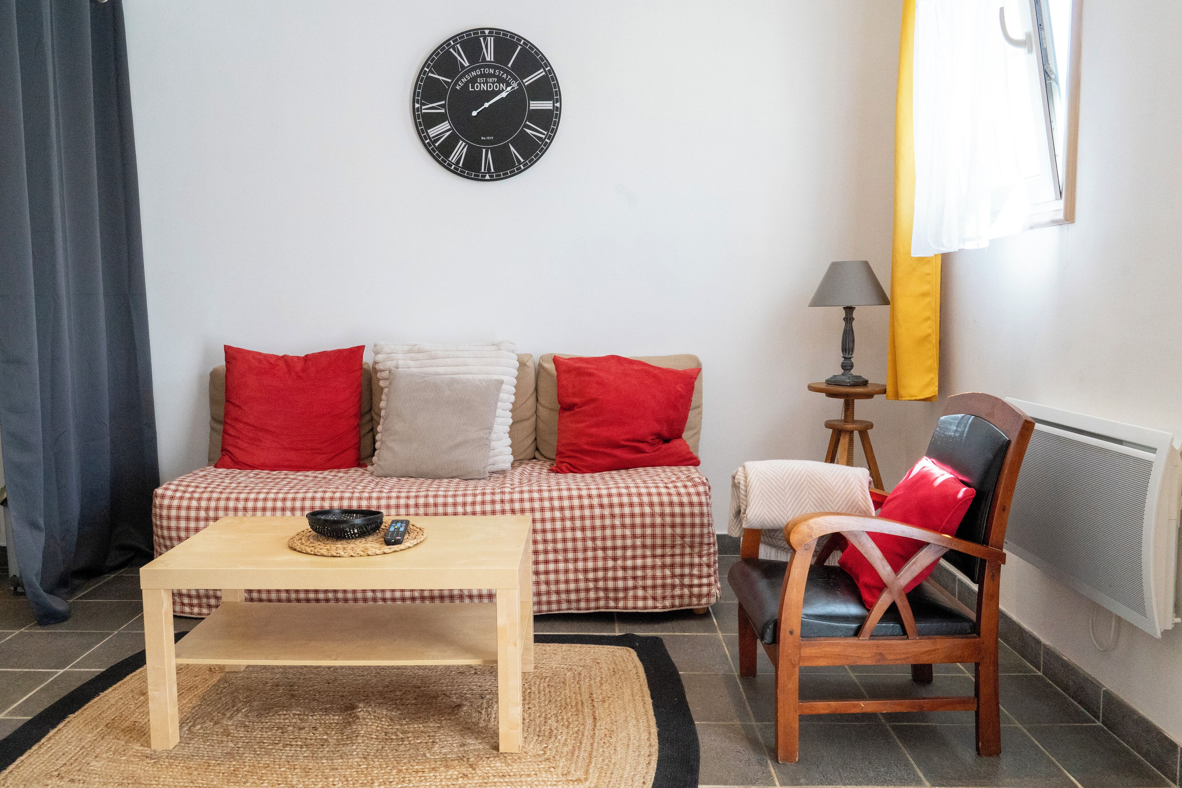 A living room with a sofa, a wooden table, a chair, a clock, and a lamp.