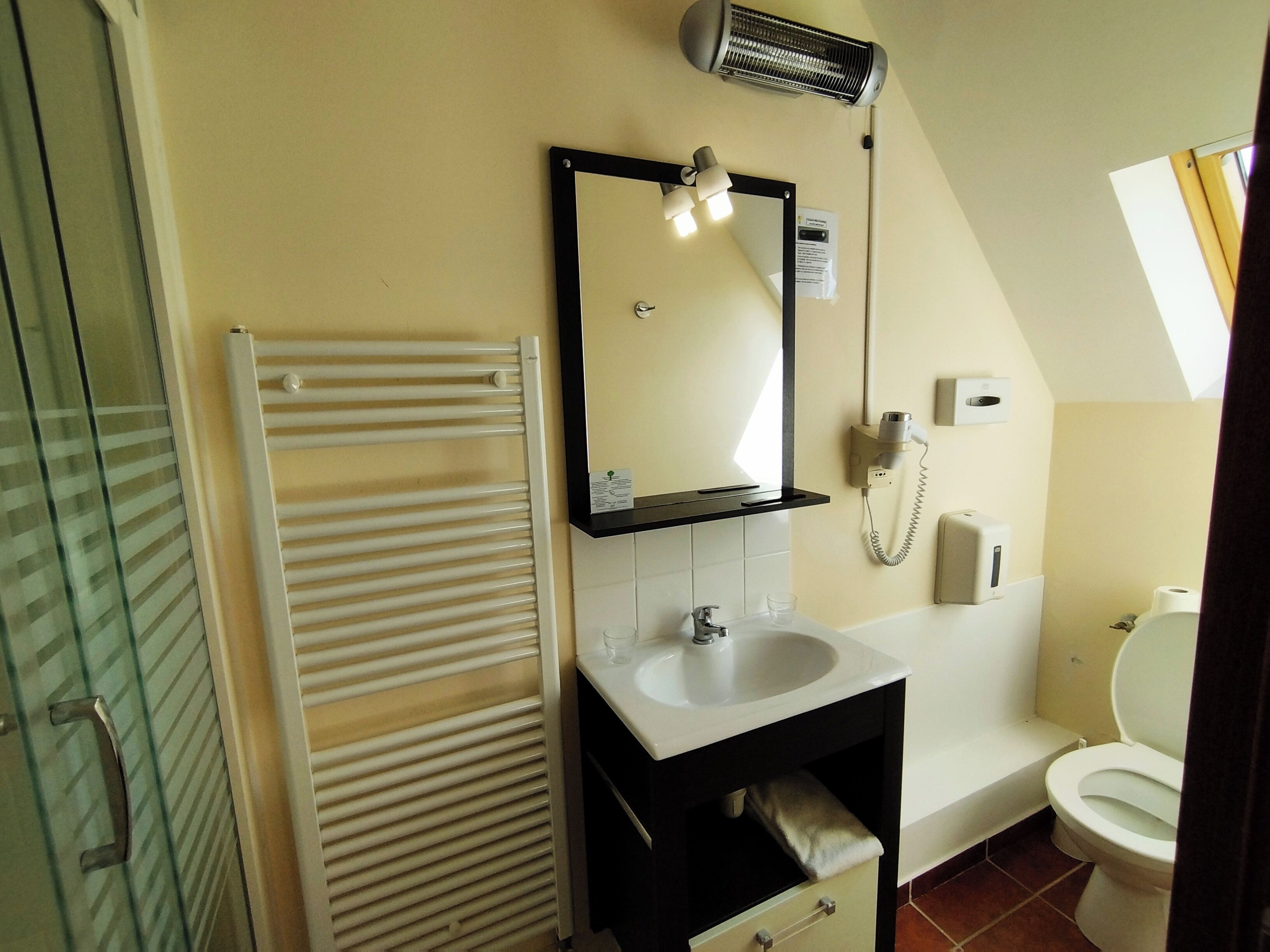 A bathroom with a white sink, a mirror, a towel rack, a heater, and a toilet.