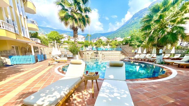 A pool area with lounge chairs and a small table, surrounded by a stone wall and palm trees. - Mountain Valley Oludeniz (Fethiye)