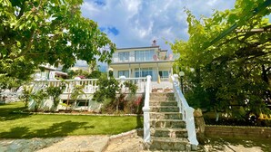 A two-story building with a white exterior, a balcony with red railings, and a stone staircase leading to the entrance. - Mountain Valley Oludeniz (Fethiye)