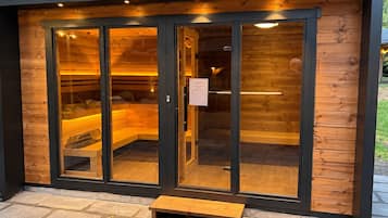 Eine Sauna mit Glastüren, einer Holzbank davor und einem Metallgitter.