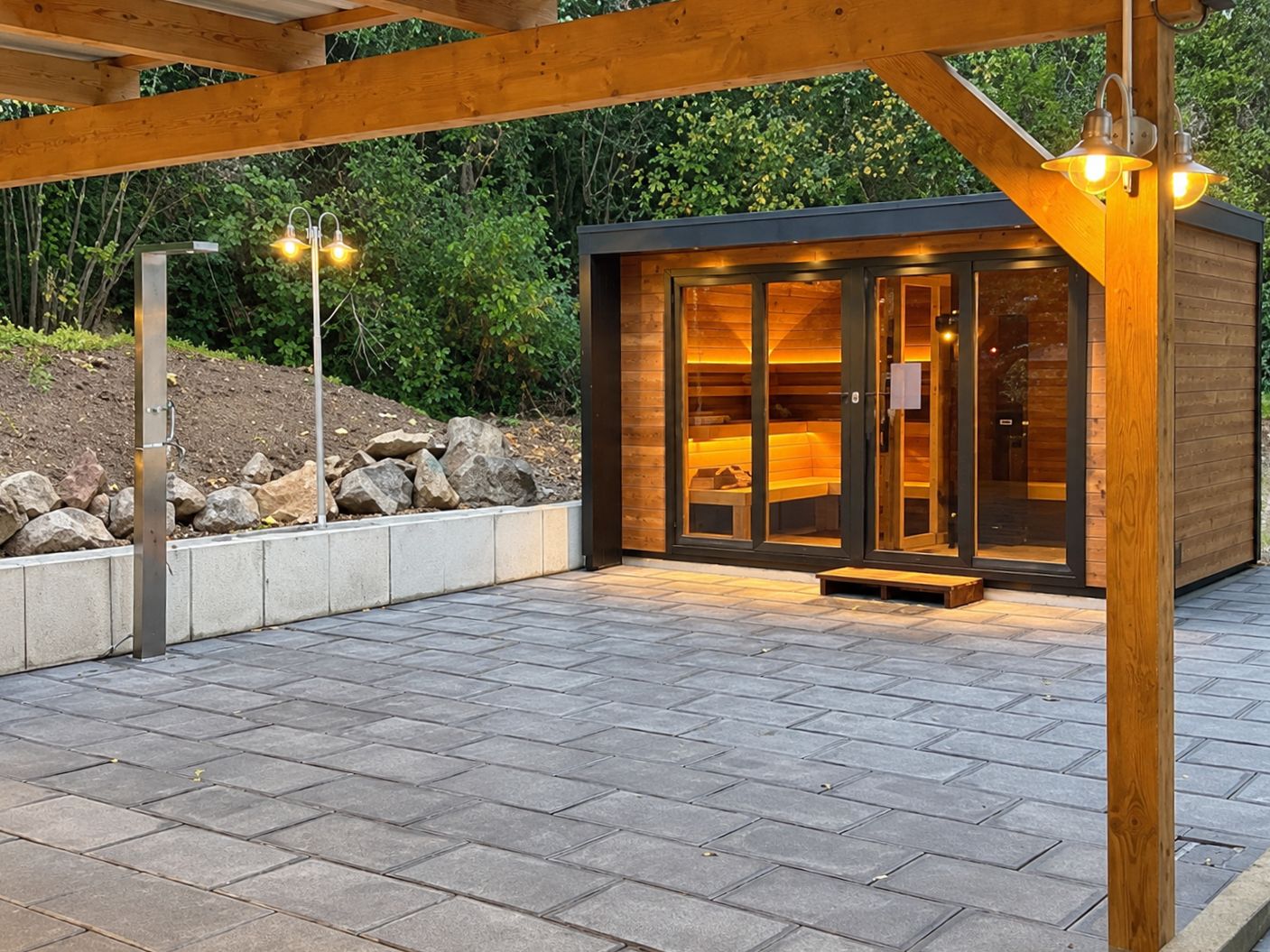 Una cabaña moderna de madera con puertas de cristal grandes, un sendero de piedra y una estructura de pérgola de madera.