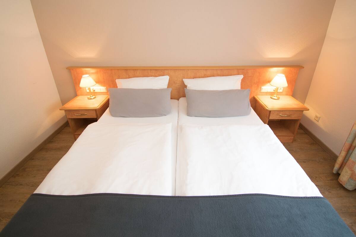 Een tweepersoonsbed met twee kussens, twee nachtkastjes met lampen, en een houten hoofdbord.
