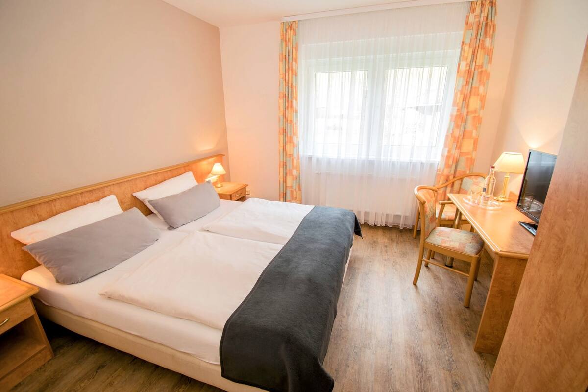 Een hotelkamer met een bed, nachtkastjes, een bureau en een stoel.