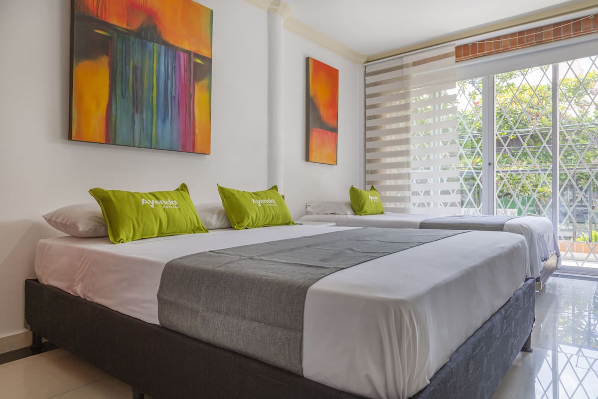 A hotel room with a large bed, two green pillows, and two abstract paintings on the wall.