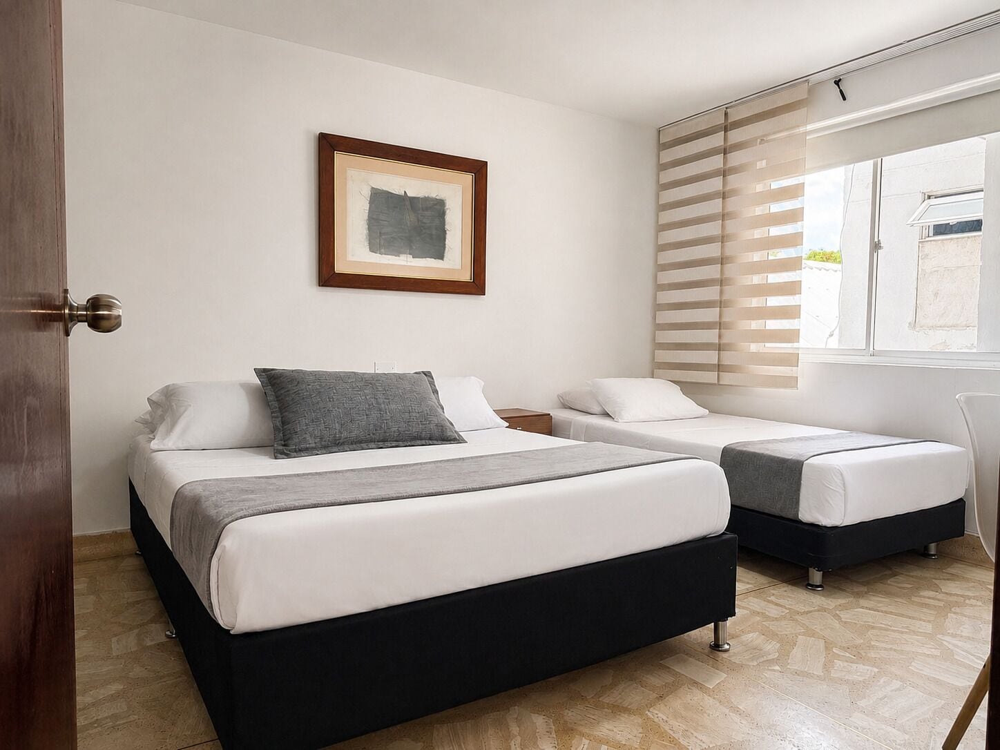 Habitación de hotel con dos camas, una obra de arte enmarcada en la pared y una ventana con persianas.
