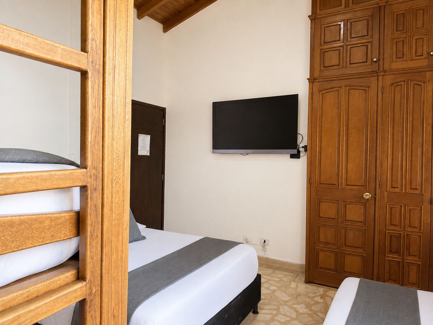A bedroom with a bed, a wardrobe, and a television on the wall.