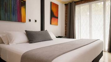 Quarto de hotel moderno com uma cama grande, uma mesa de cabeceira, uma luminária e uma janela com cortinas.