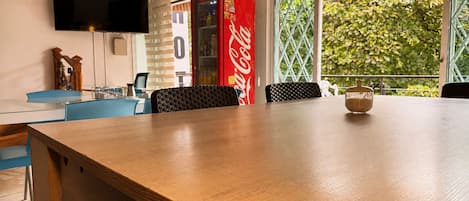 Una sala de conferencias con una mesa de madera, sillas azules, un televisor en la pared y un refrigerador Coca-Cola.