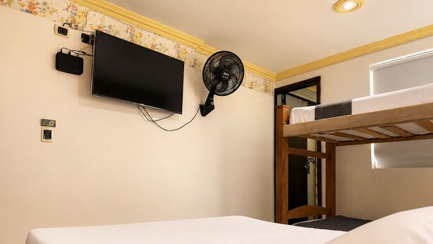 Une chambre avec un lit superposé, un téléviseur fixé au mur et un ventilateur.