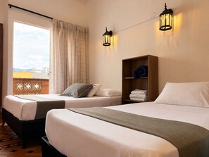 Una habitación de hotel con dos camas, un estante de madera con toallas y dos luces fijadas a la pared.
