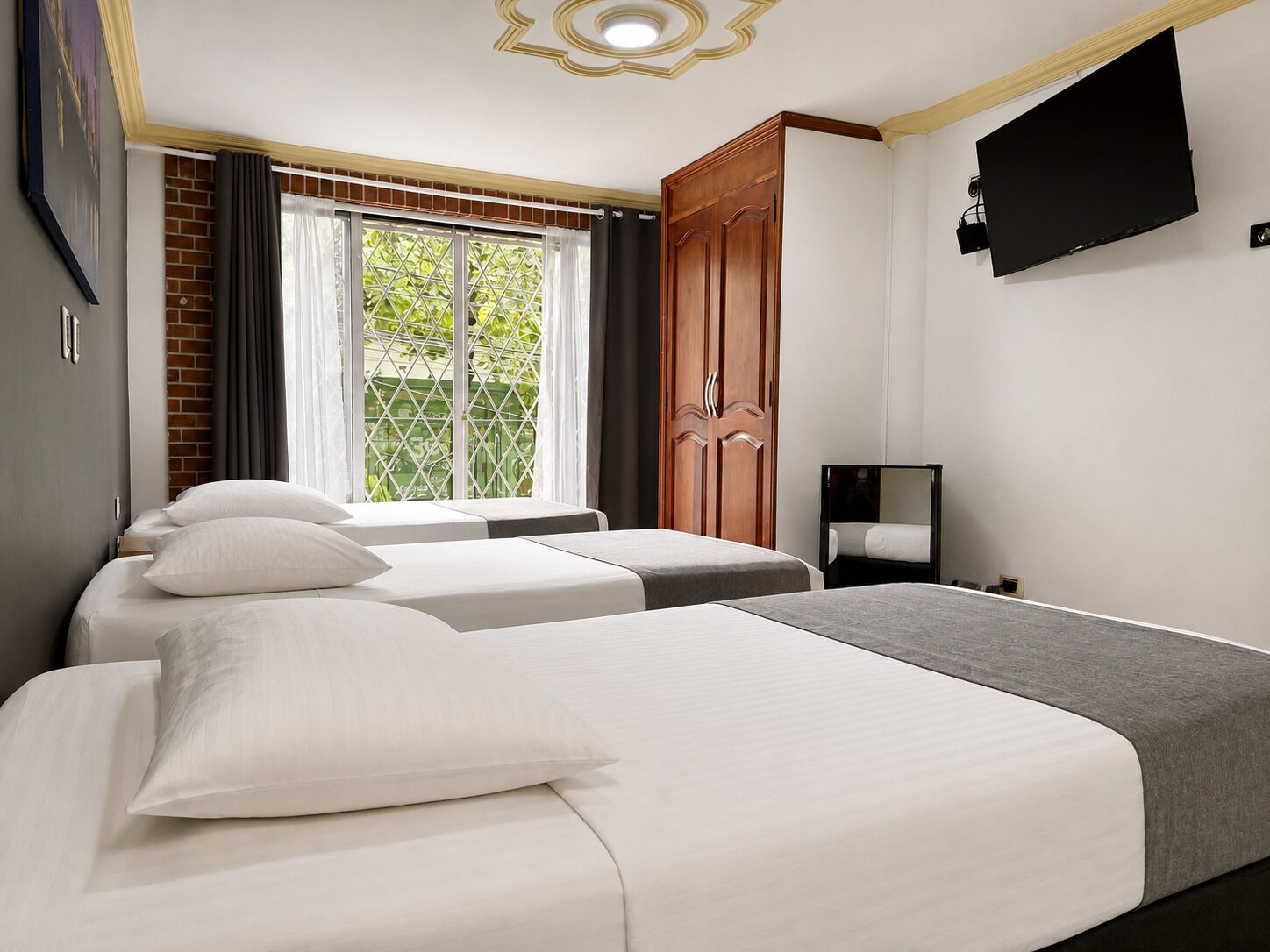 Una camera d'albergo con due letti, una televisione montata a parete e una finestra con tende.