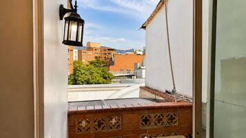 Un balcón con un muro de ladrillo, un farol colgante y vistas a edificios y árboles.