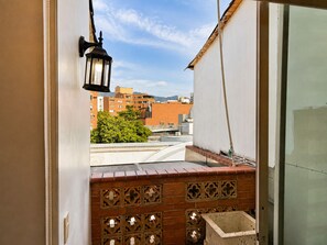 A balcony with a brick wall, a hanging lantern, and a view of buildings and trees. - Hotel Boutique Laureles Home (Medellín)