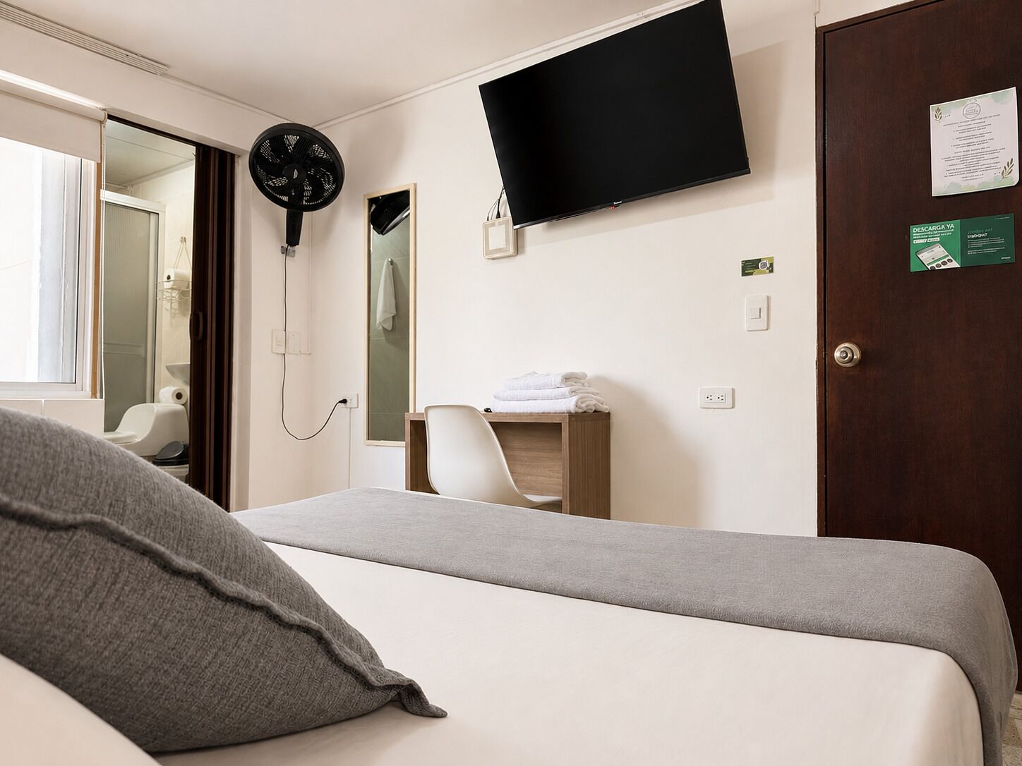 Ein Hotelzimmer mit Bett, Flachbildfernseher, Spiegel, Handtuchhalter und Tür.