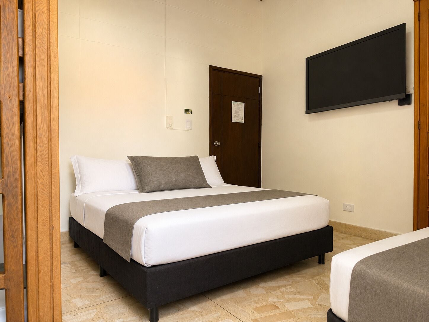 A hotel room with a bed, a television mounted on the wall, and a door.