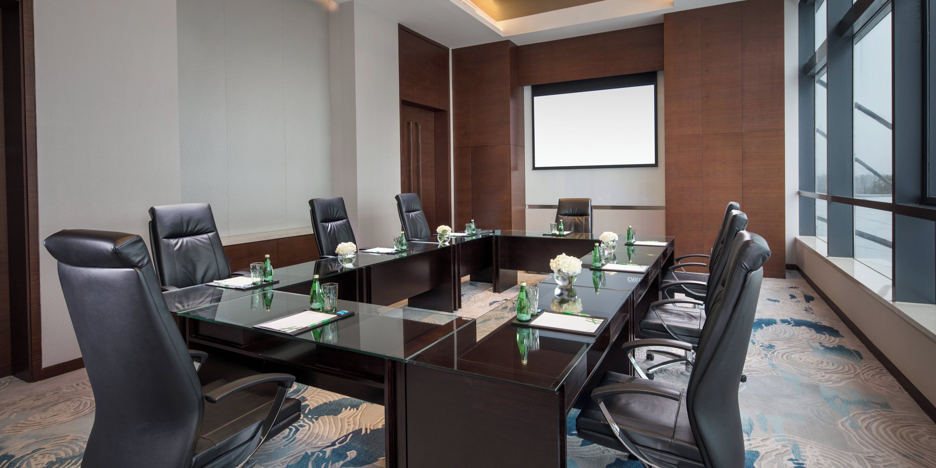 A conference room with a glass table, leather chairs, and a projector screen.