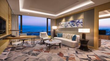 A modern hotel room with a large window offering a city view, a sofa, a coffee table, and a TV.