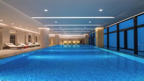 A long indoor swimming pool with a tiled floor, surrounded by lounge chairs and a glass wall on one side. - Holiday Inn Suzhou Taihu Lake by IHG (Suzhou)