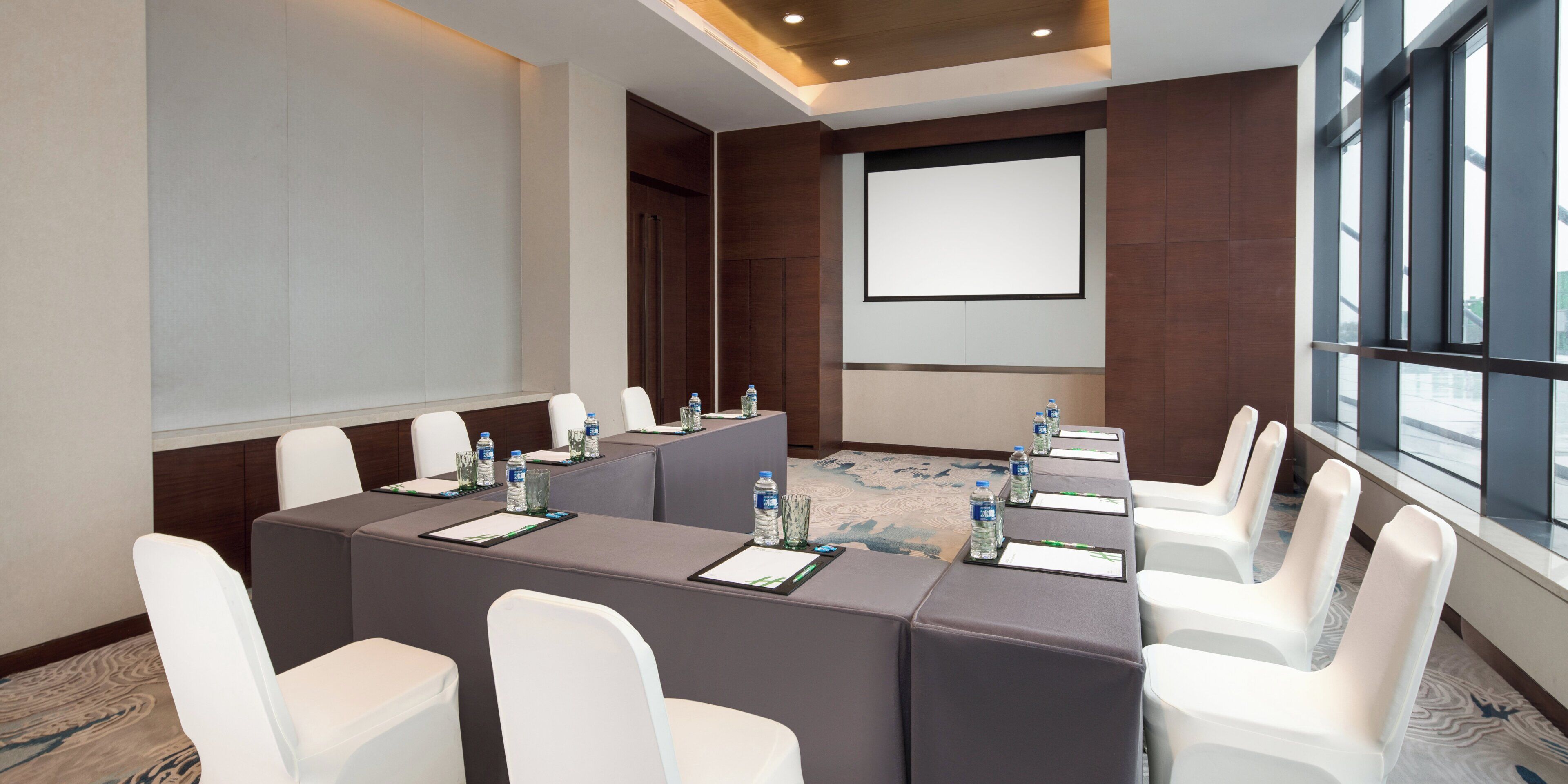 A conference room with a long table, white chairs, water bottles, and a projector screen.