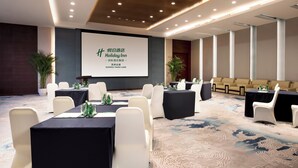 Un salón de conferencias con mesas, sillas y una pantalla de proyección mostrando texto.