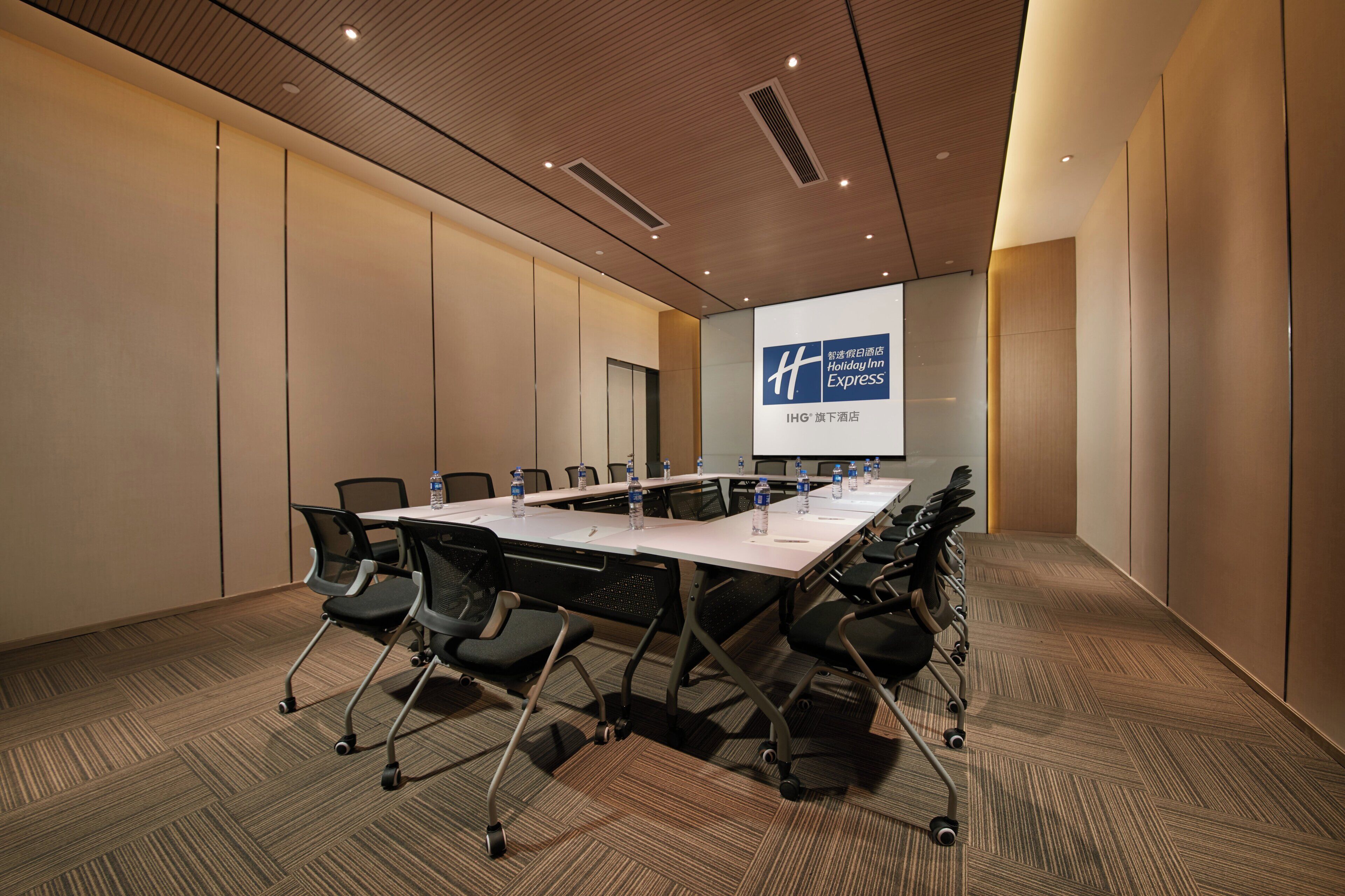 A conference room with a long table, chairs, and a projector screen displaying a hotel name.