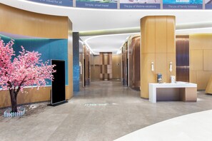 A modern hotel lobby with a reception desk, a large digital screen, and a decorative cherry blossom tree.