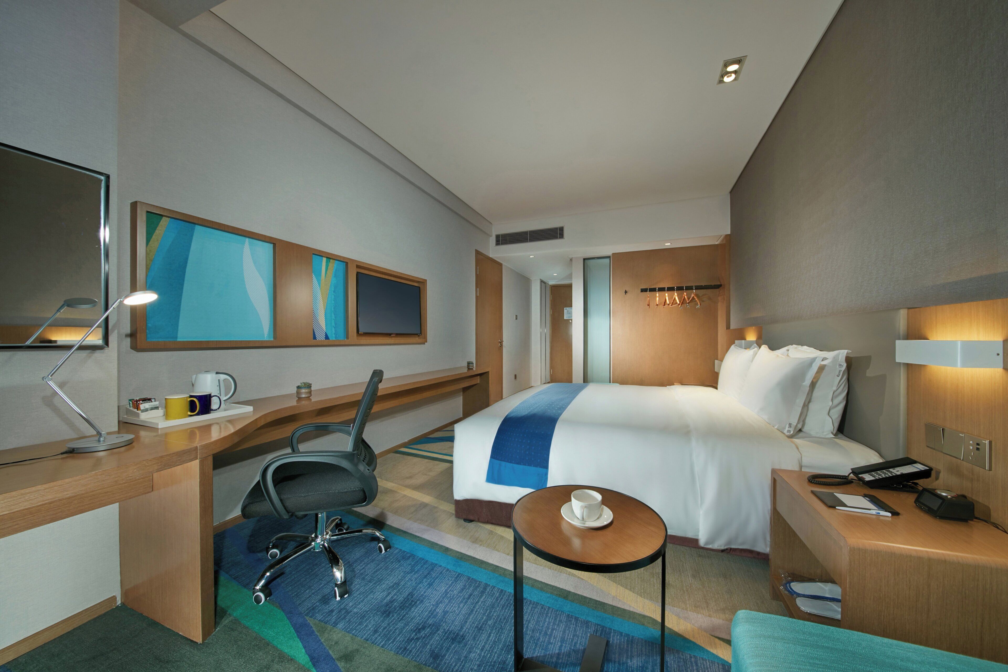 A hotel room with a bed, desk, chair, bedside table, and a small round table.