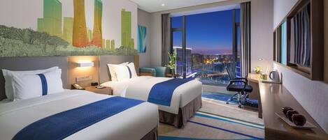 Ein Hotelzimmer mit zwei Betten, einem Schreibtisch, einem Stuhl, einem Nachttisch, einer Lampe und einem großen Fenster mit Blick auf die Stadt.