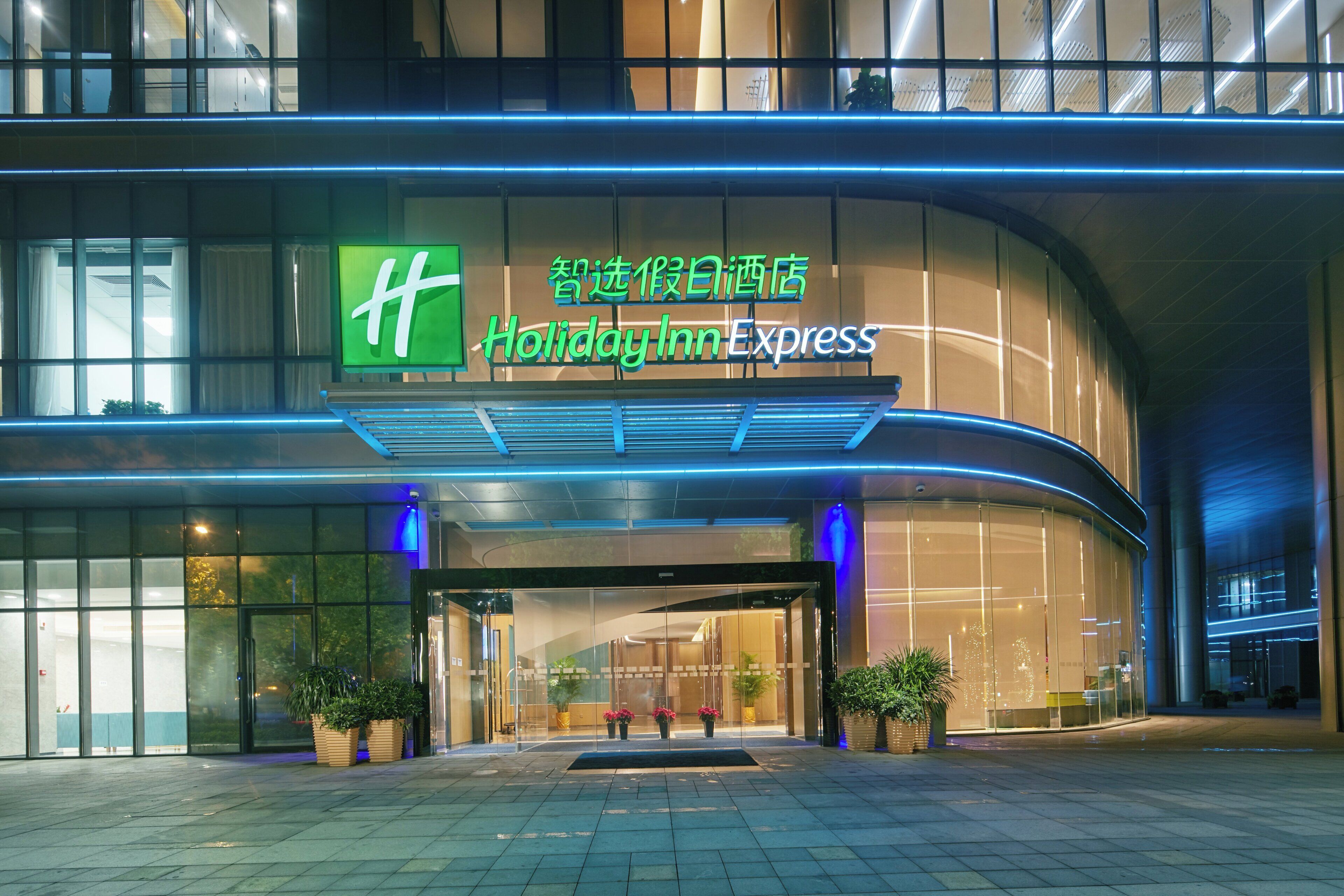 A Holiday Inn Express hotel entrance with a modern design, large glass windows, and a prominent green logo.