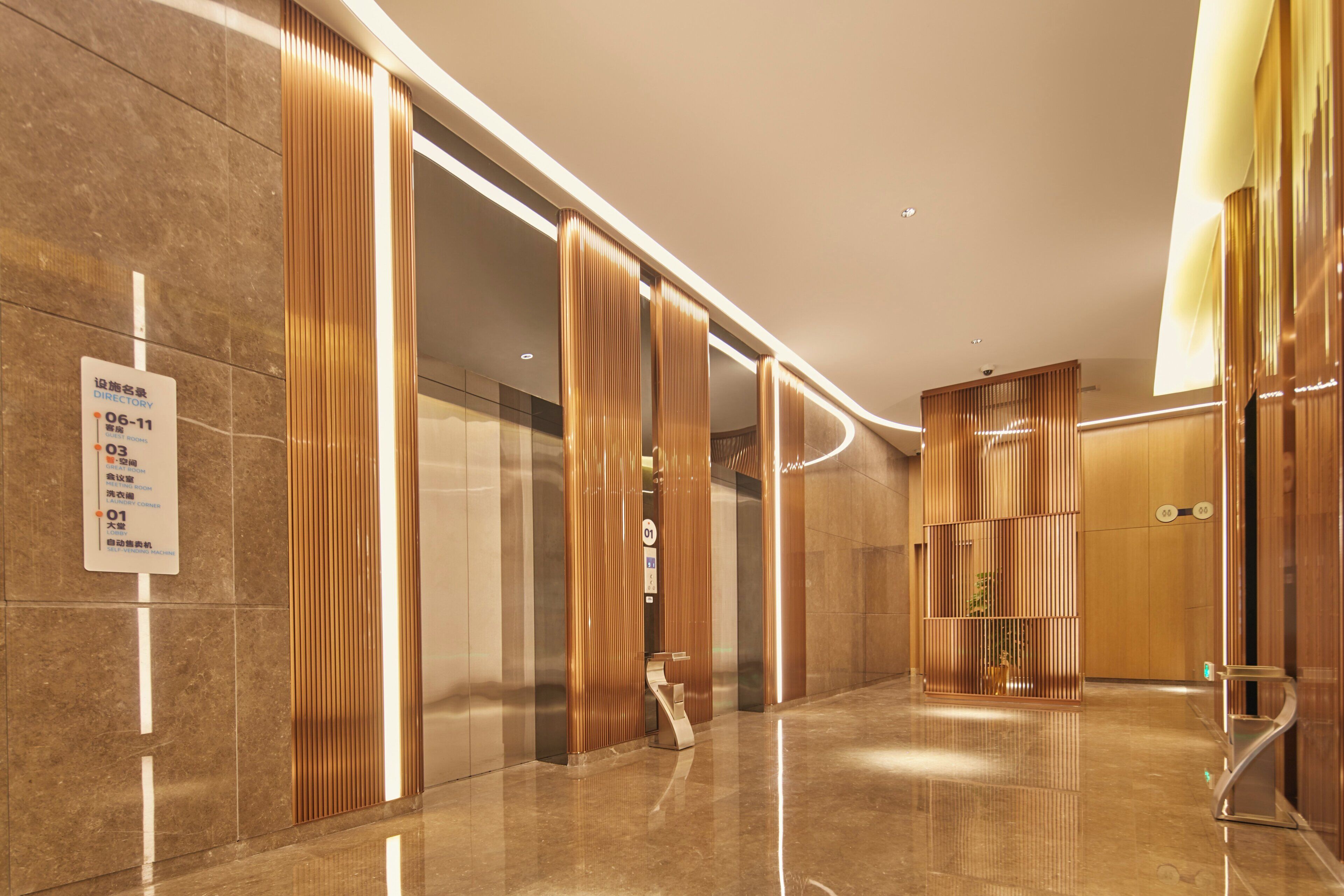 A modern hotel lobby with a directory sign, a self-service vending machine, and a well-lit corridor.