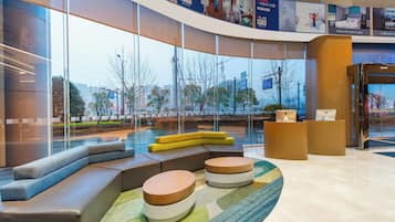 A modern lobby with seating areas, a reception desk, and large windows offering views of the outside.