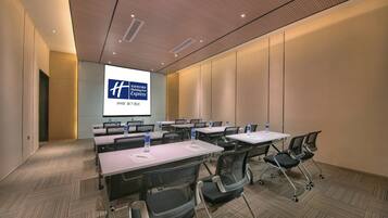 A conference room with a large screen displaying a hotel logo, multiple tables with chairs, and a carpeted floor.