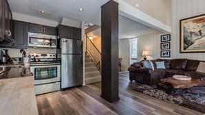 Una cocina moderna con electrodomésticos de acero inoxidable, piso de madera y un pilar marrón oscuro.